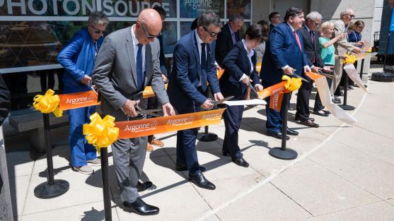 A group of people standing in a row cutting a large ribbon.