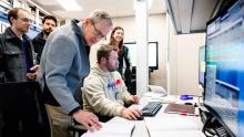 A group of scientists look at screens in a control room.